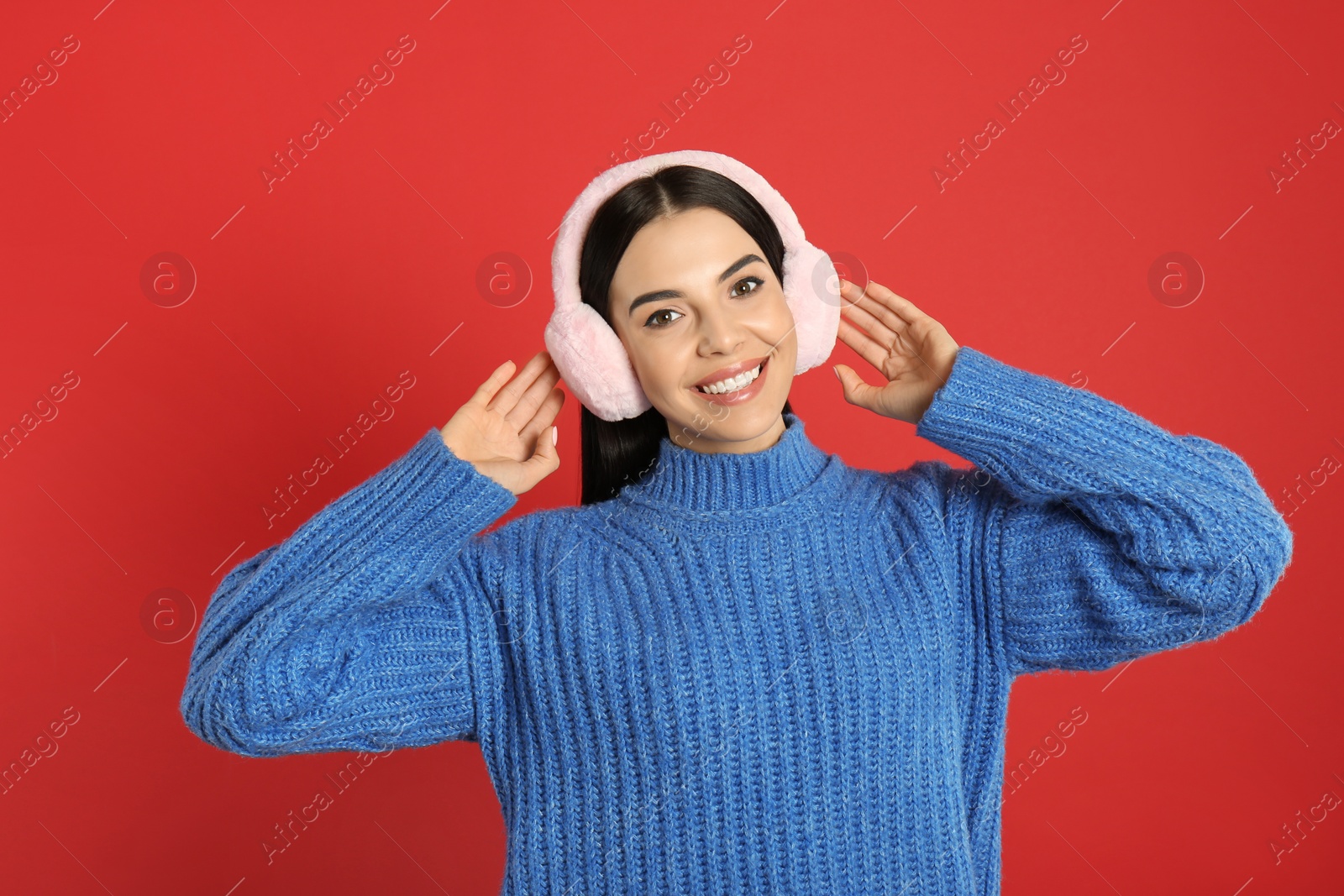 Photo of Beautiful young woman wearing earmuffs on red background