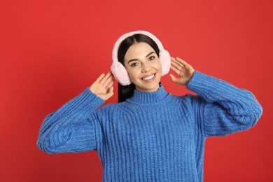 Beautiful young woman wearing earmuffs on red background