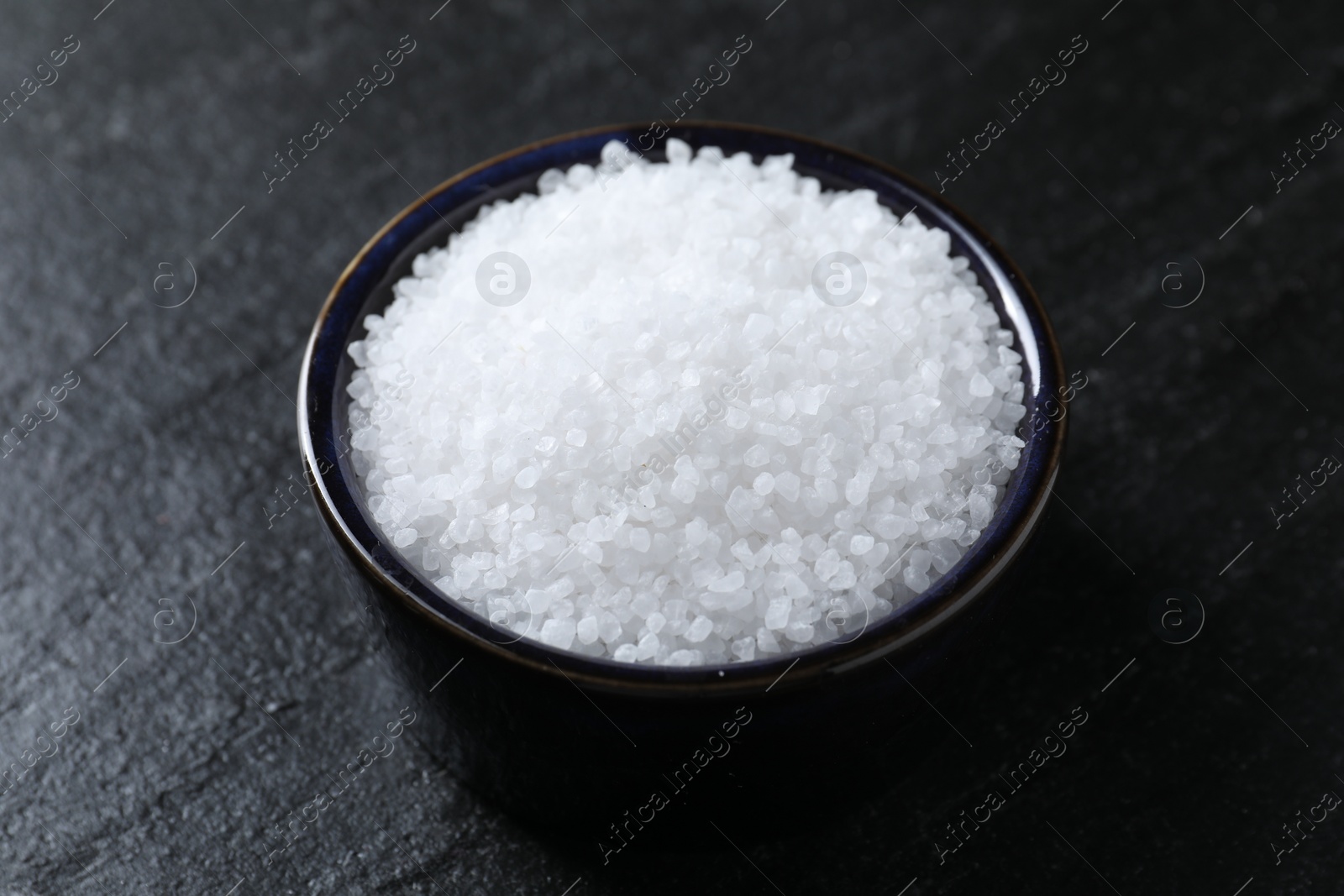 Photo of Organic white salt in bowl on black table