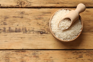 Photo of Raw basmati rice in bowl and scoop on wooden table, top view. Space for text