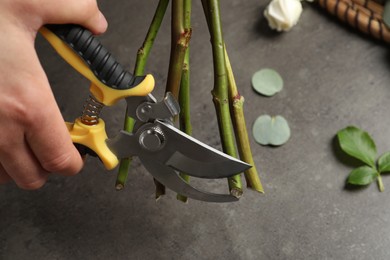 Photo of Florist cutting flower stems with pruner at grey stone table, closeup