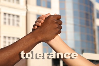Image of Tolerance, support and cooperation concept. Men of different races clasping hands on city street, closeup