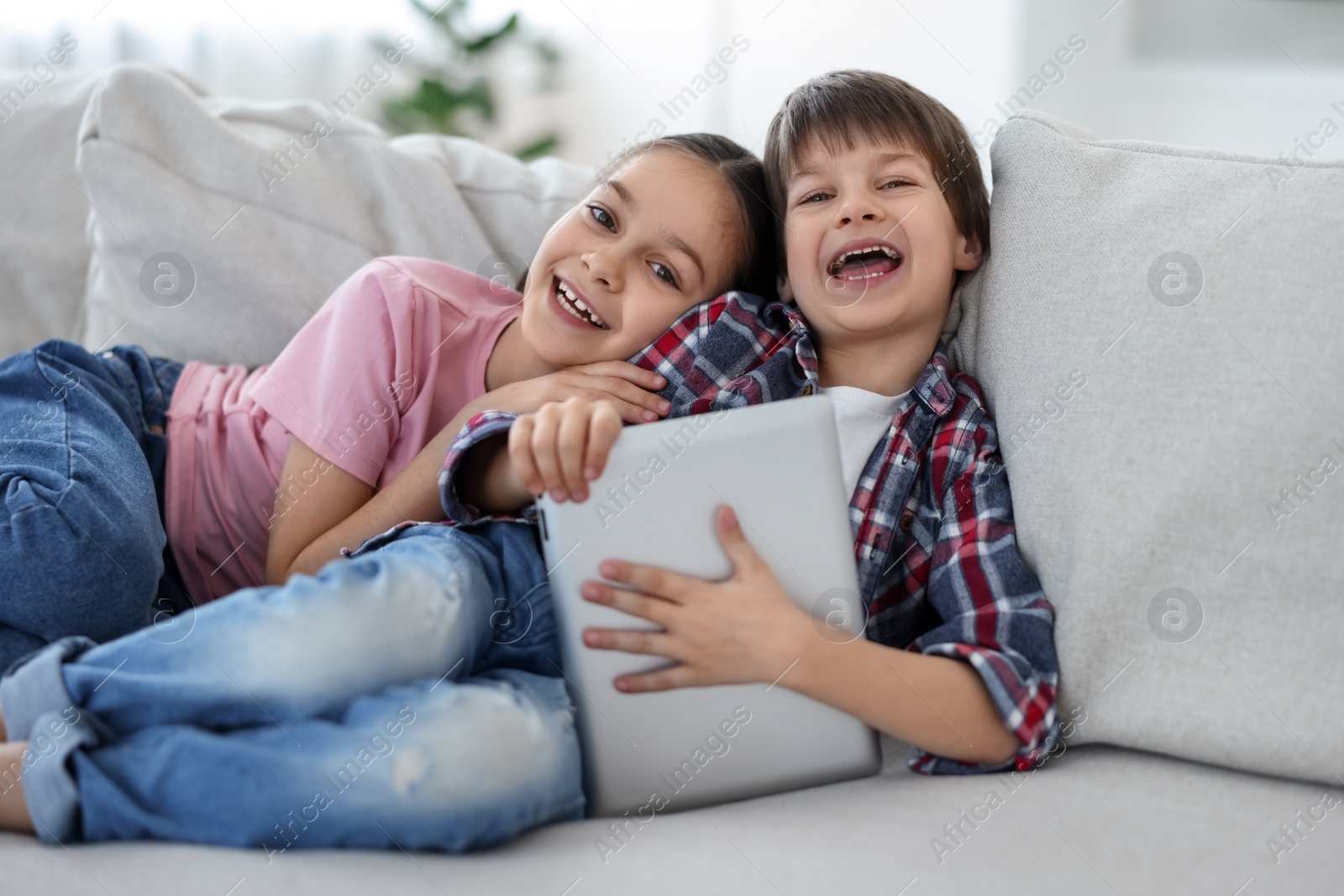 Photo of Happy brother and sister with tablet on sofa at home