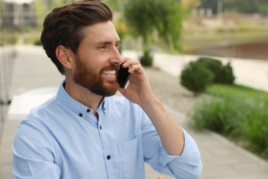 Photo of Handsome man talking on phone outdoors, space for text