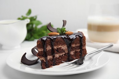 Photo of Piece of tasty homemade chocolate cake with mint and almonds on white table, closeup