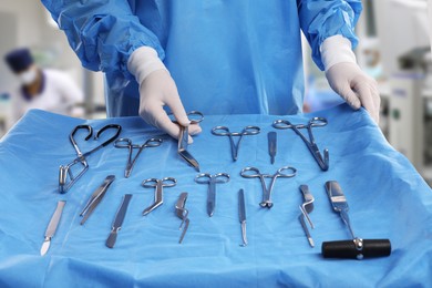 Nurse near table with different surgical instruments in operating room, closeup