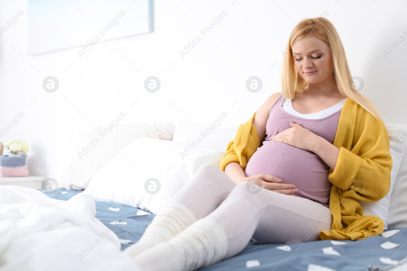 Photo of Beautiful pregnant woman resting on bed in light room. Space for text