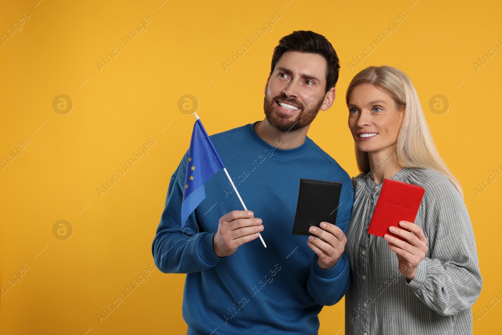 Photo of Immigration. Happy couple with passports and flag of European Union on orange background, space for text