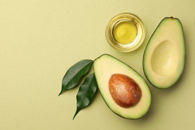 Cooking oil in bowl and fresh avocados on light green background, flat lay. Space for text