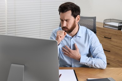 Photo of Sick man coughing at workplace in office. Cold symptoms