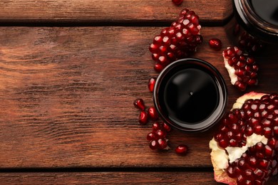 Photo of Glass bowl of tasty pomegranate sauce and fresh ripe fruit on wooden table, flat lay. Space for text