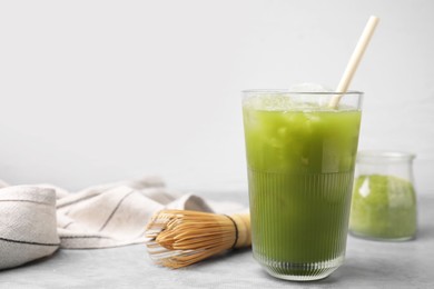 Photo of Glass of delicious iced green matcha tea and bamboo whisk on light grey table, space for text