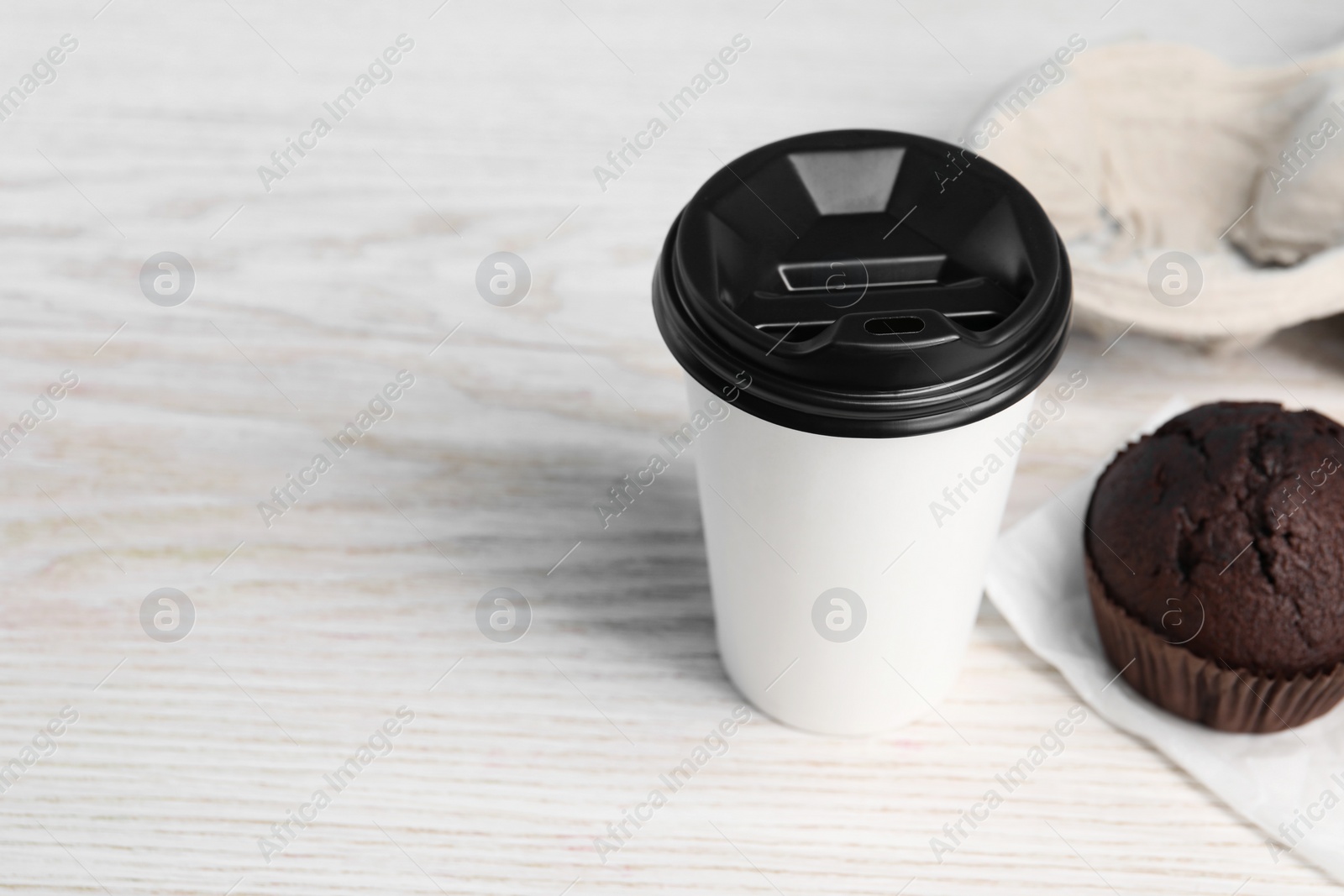 Photo of Paper cup and muffin on white wooden table, space for text. Coffee to go