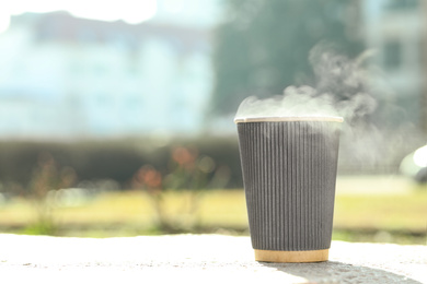 Paper coffee cup with hot drink outdoors. Space for text