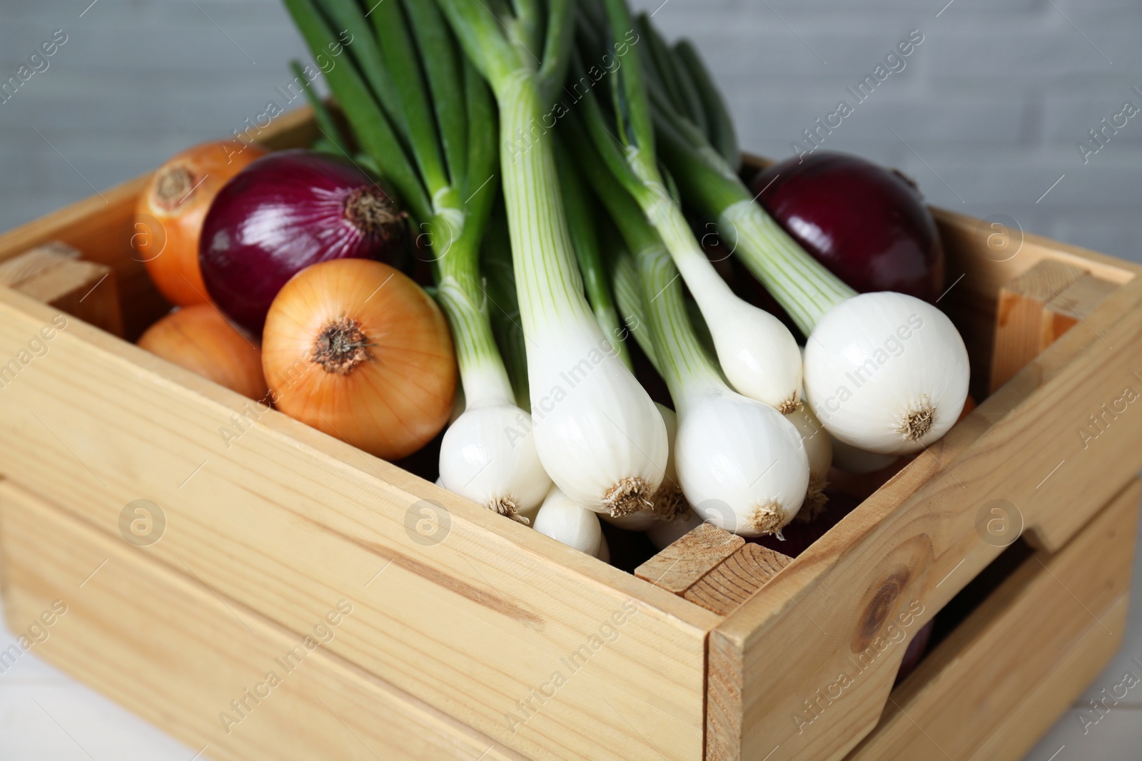 Photo of Crate with different kinds of onions on table, closeup