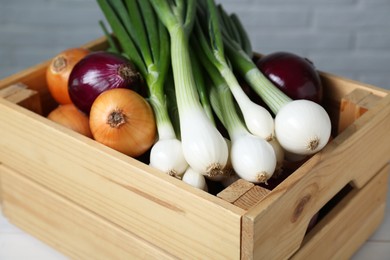 Crate with different kinds of onions on table, closeup