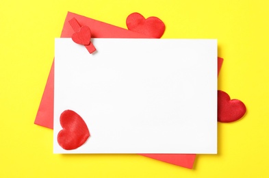 Photo of Blank card, envelope and red decorative hearts on yellow background, flat lay with space for text. Valentine's Day celebration