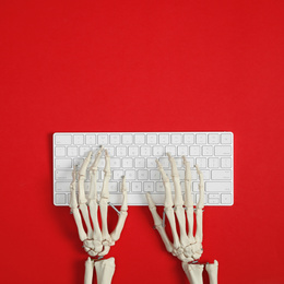 Photo of Human skeleton using computer keyboard on red background, top view. Space for text