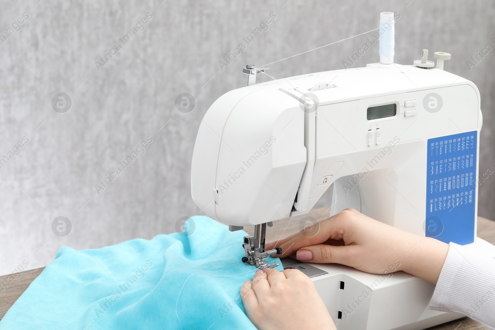 Photo of Seamstress working with sewing machine at table indoors, closeup