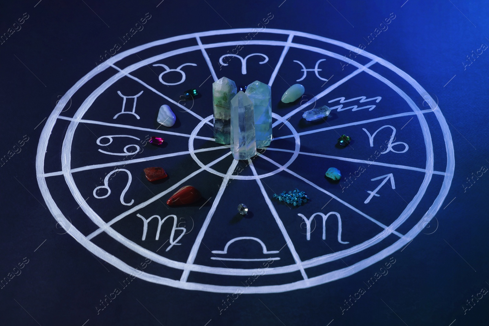 Photo of Natural stones for zodiac signs and drawn astrology chart on dark blue background