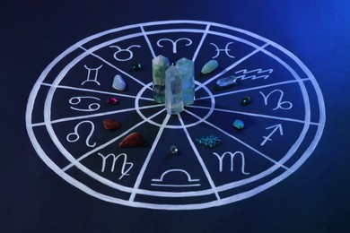 Photo of Natural stones for zodiac signs and drawn astrology chart on dark blue background