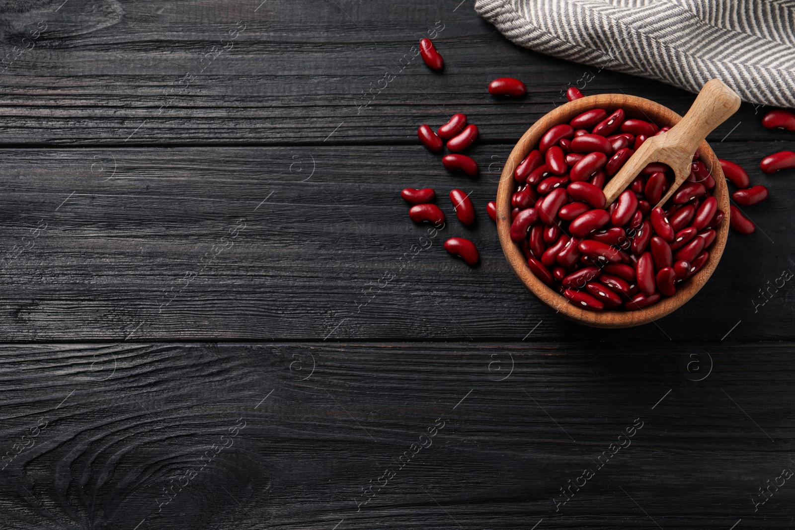 Photo of Raw red kidney beans with bowl, scoop and napkin on dark wooden table, flat lay. Space for text