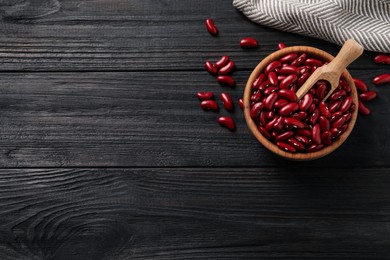 Photo of Raw red kidney beans with bowl, scoop and napkin on dark wooden table, flat lay. Space for text