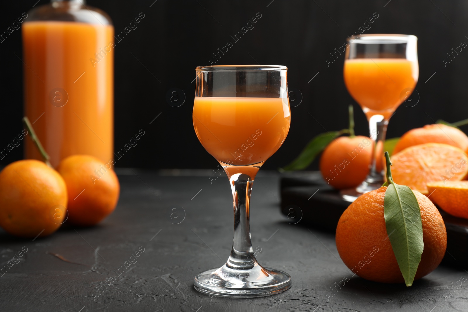 Photo of Tasty tangerine liqueur and fresh fruits on black textured table