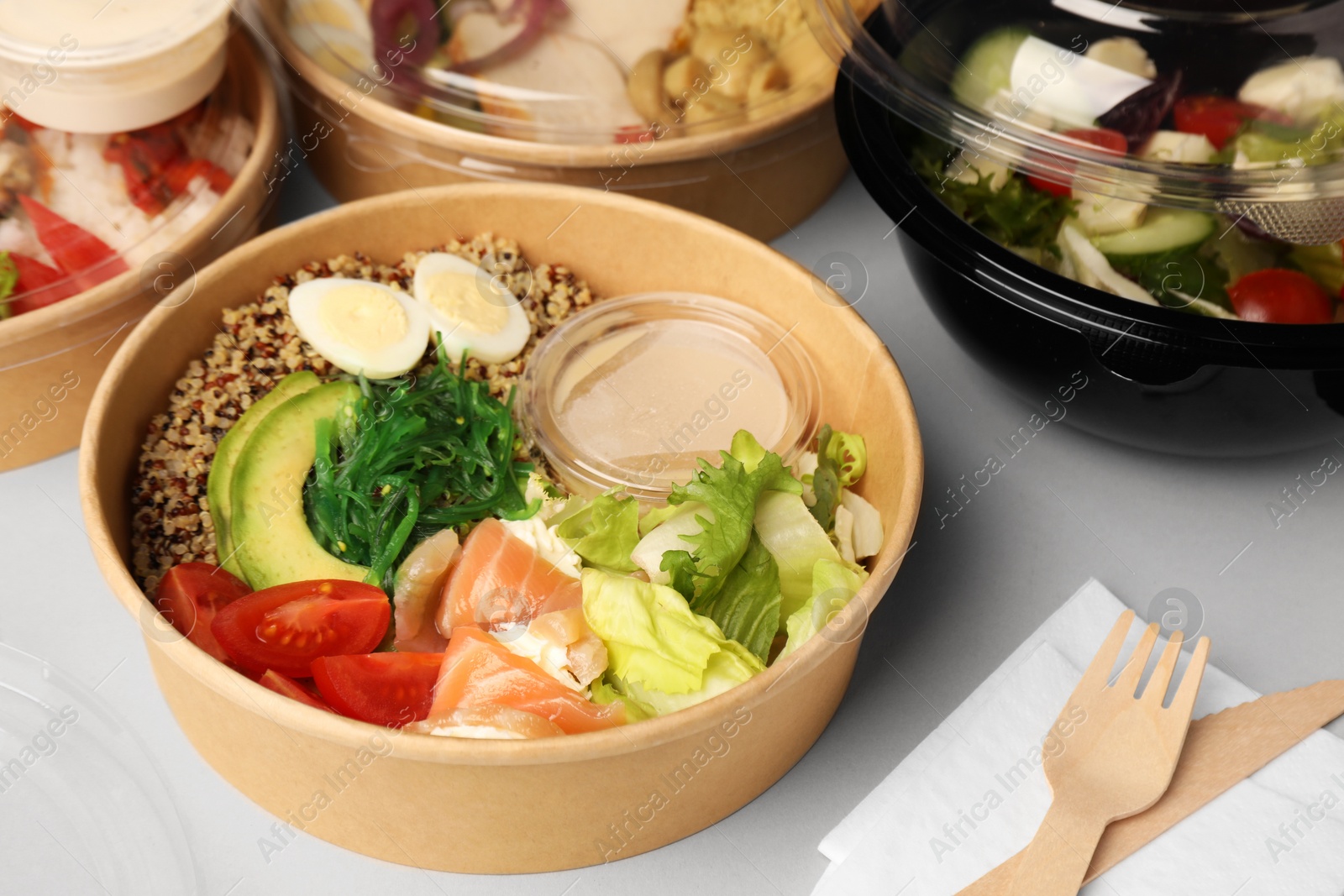 Photo of Tasty food in containers with wooden knife and fork on light grey table