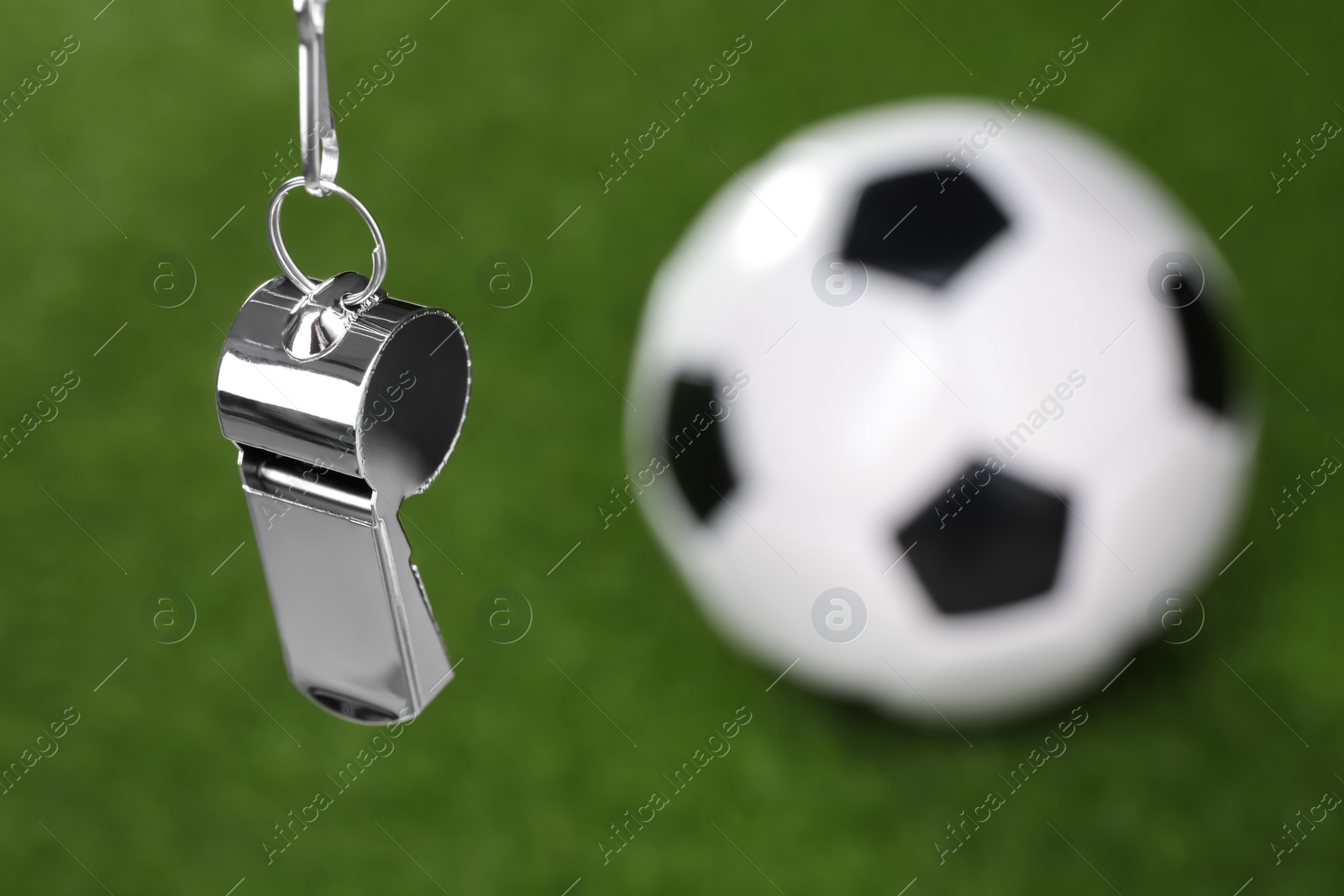 Photo of Football referee equipment. Metal whistle and soccer ball on green grass, closeup with space for text