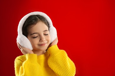 Photo of Cute girl wearing stylish earmuffs on red background. Space for text