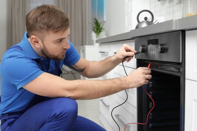 Photo of Professional serviceman repairing modern oven in kitchen