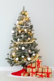 Photo of Decorated Christmas tree with red skirt and gifts indoors