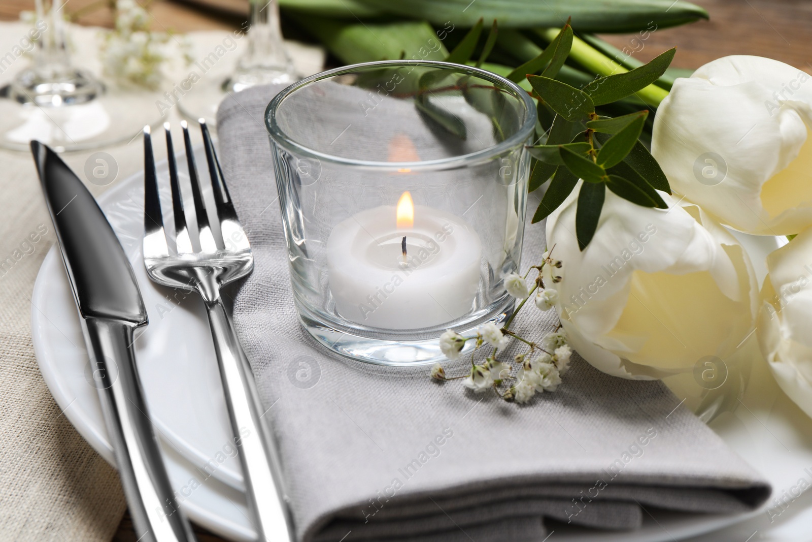 Photo of Stylish setting with cutlery, burning candle and tulips on table, closeup