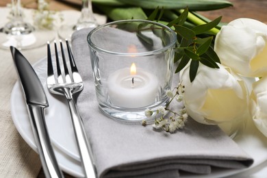 Stylish setting with cutlery, burning candle and tulips on table, closeup