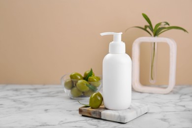 Photo of Bottle of cosmetic product with olive essential oil on white marble table, space for text