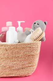 Photo of Wicker basket full of different baby cosmetic products, hairbrush and toy on pink background, closeup