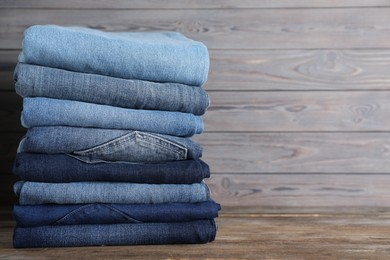 Photo of Stack of different jeans on wooden table. Space for text