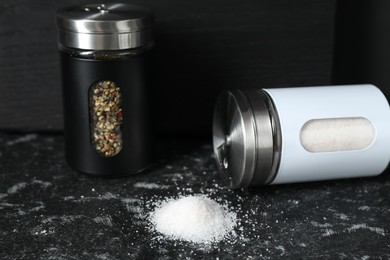 Photo of Salt and pepper shakers on dark table, closeup