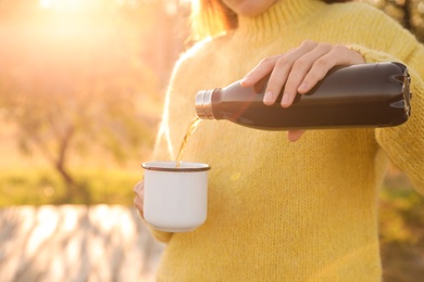 Woman pouring hot drink from thermos bottle into cup outdoors, closeup