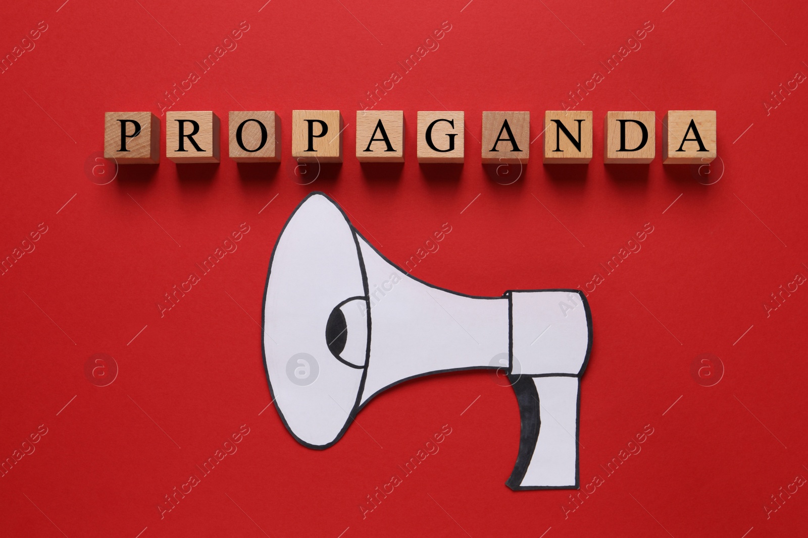 Photo of Word Propaganda made of wooden cubes and paper loudspeaker on red background, flat lay. Information warfare concept