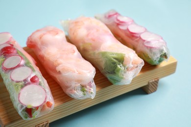 Photo of Different delicious spring rolls wrapped in rice paper on light blue background, closeup