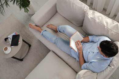 Photo of Man reading book on sofa in living room, above view