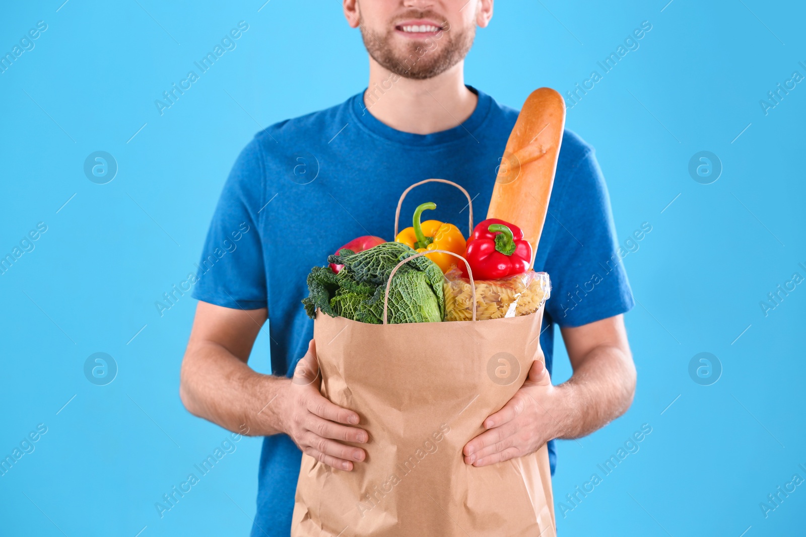 Photo of Delivery man holding paper bag with food products on color background, closeup