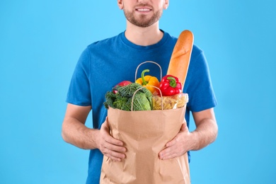 Delivery man holding paper bag with food products on color background, closeup