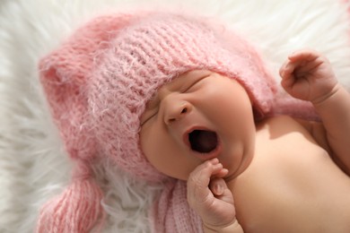 Photo of Cute newborn baby in hat yawning on fuzzy blanket, closeup