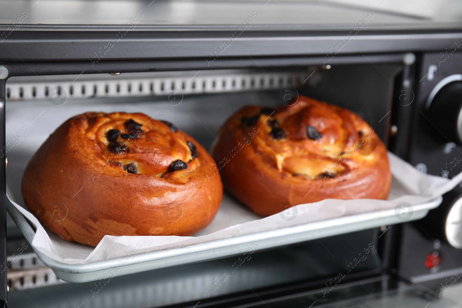 Photo of Delicious rolls with raisins on baking tray in oven, closeup. Cooking sweet buns