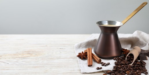 Image of Turkish coffee. Cezve with freshly brewed beverage, cinnamon, anise, coffee beans and chocolate on white wooden table. Banner design with space for text