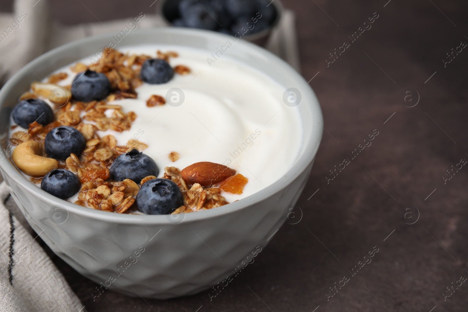 Photo of Bowl with yogurt, blueberries and granola on grey table, closeup. Space for text