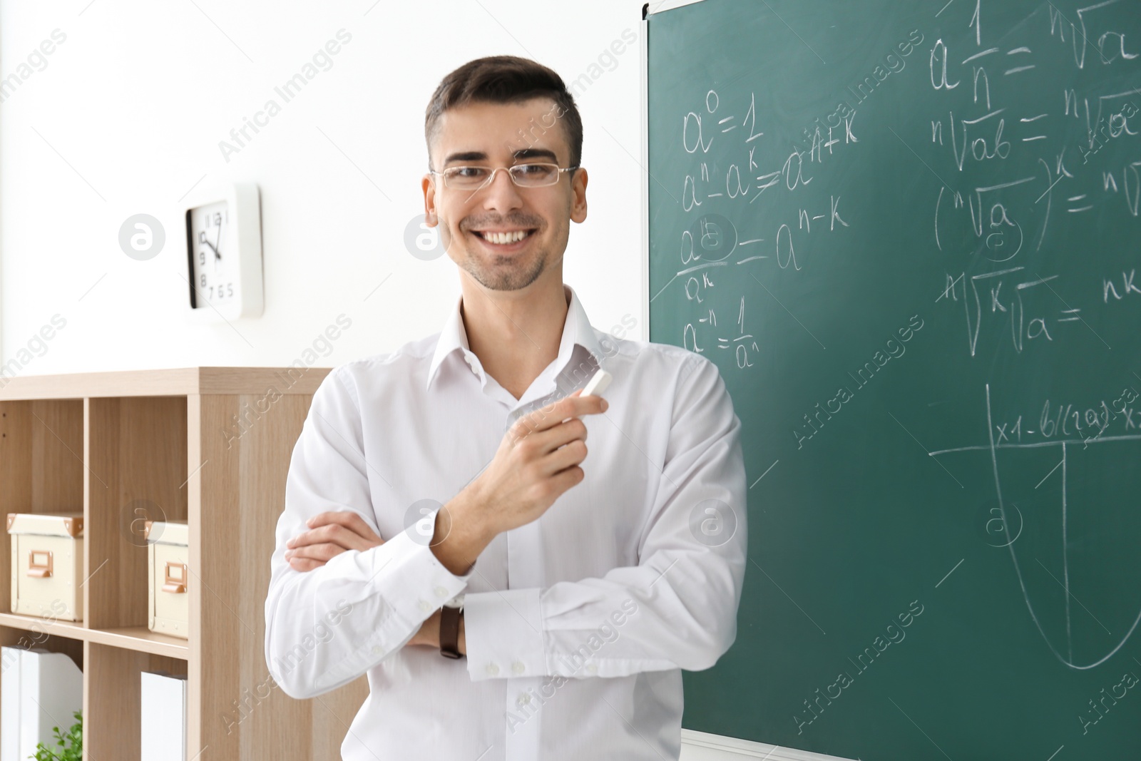 Photo of Young male teacher with chalk near blackboard in classroom